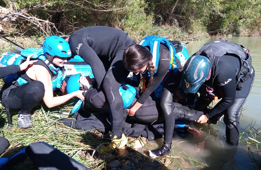 Grupo de rescatadores con neopreno y casco realizando la extracción de una víctima en un río de aguas bravas. 